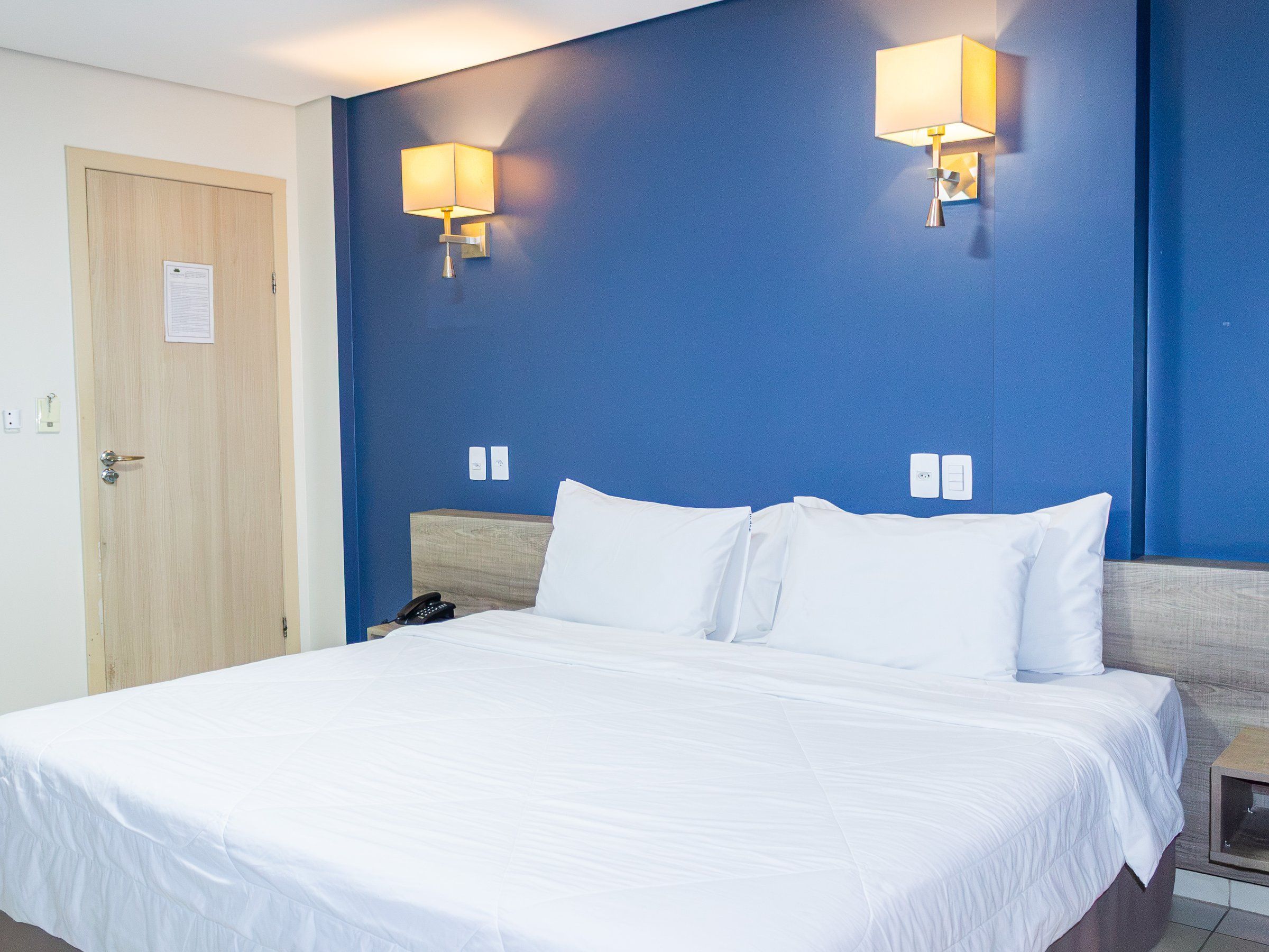 Deluxe Single room, double bed with a blue wall and two wall lamps